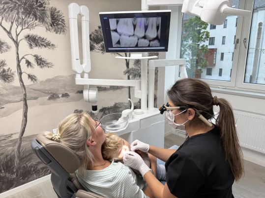 Zahnärztin untersucht ein Kind auf dem Schoß der Mutter im Behandlungszimmer.